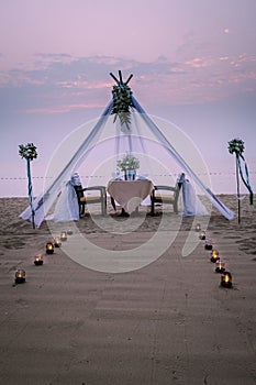 Young couple Honeymoon dinner by candle light during sunset on the beach, men and woman having dinner on the beach