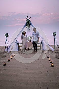 Young couple Honeymoon dinner by candle light during sunset on the beach, men and woman having dinner on the beach