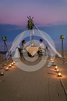 Young couple Honeymoon dinner by candle light during sunset on the beach, men and woman having dinner on the beach