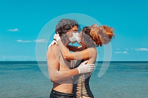 Young couple hugging and kissing through the face masks on the beach