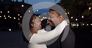 Young couple hugging and looking to camera. Close up of smiling boyfriend and girlfriend standing together at night city