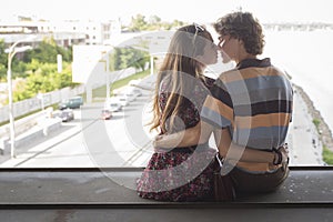 Young couple hugging in the summer daylight on a bridge construction in the city outdoors. copy space