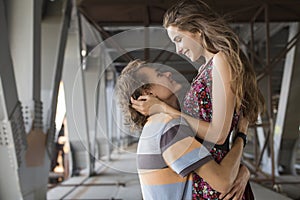 Young couple hugging in the summer daylight on a bridge construction in the city outdoors. copy space