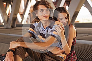 Young couple hugging in the summer daylight on a bridge construction in the city outdoors. copy space