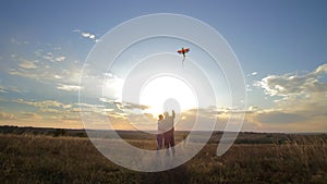 A young couple hugs in the park at sunset and fly a kite on a sunny day. Silhouette of a man and a girl. A colored plane