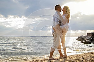 A young couple hugs passionately on the deserted sandy shore. Lifestyle of passionate newlyweds by the ocean. Love, passion and
