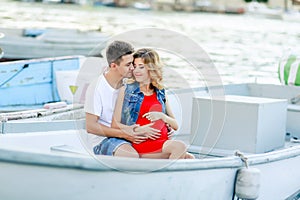 Young couple hugs and relaxing at dock near boat, on sunny summer day. Woman and man in fashionable clothes stands near