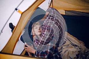 Young couple hugs in tent during winter hike. Guy sits, girl lies on guy`s knees.