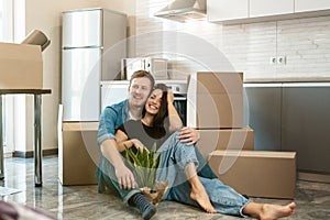 Young couple husband and wife looking happy having break sitting on the kitchen floor during moving to new appartment unpacking
