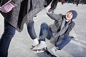 Young couple at ice rink, woman helping man up after falling