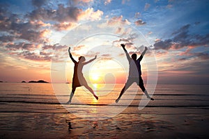 Young couple in a jump on the sea beach at sunset