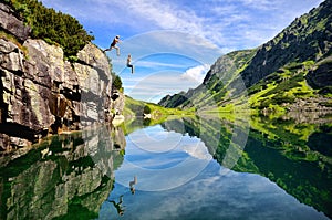 Young couple jump together into lake in mountains with beautiful blue water and reflexion