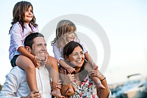 Young couple with kids on shoulders outdoors.