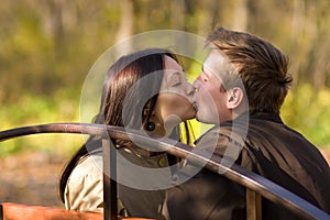 Young couple kiss on a bench in park