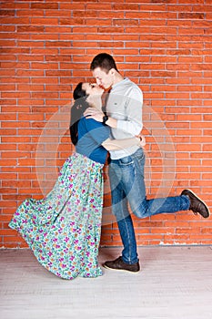 Young couple kiss in front of red brick wall.