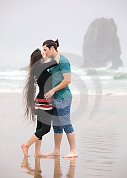 Young couple kissing on beach by ocean on foggy day