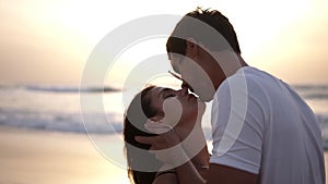 Young couple kissing and bonding at sunset on beach. Loving man and woman hugging in bright rays of sun on background of
