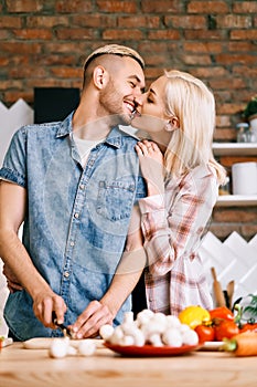 Young couple kissing and cooking together vegetarian meal in the kitchen at home