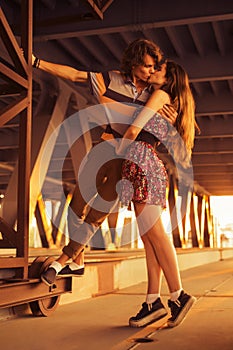 Young couple kissing in the flares of sunset light on a bridge c