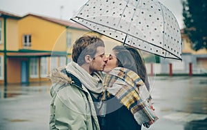 Young couple kissing outdoors under umbrella in a rainy day