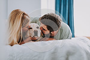 Young couple kissing their dog in bed