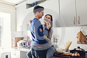 Young couple in the kitchen hugging and eating cheese.