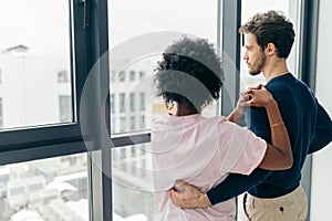 Romantic mixed race couple standing by the window thinking about their future.