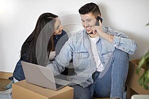 Young Couple With Laptop And Cellphone Purchasing Furniture Online After Moving Home