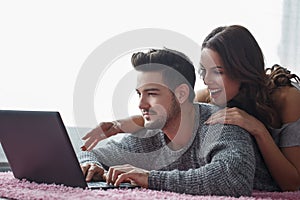Young couple with laptop lying prone on carpet photo