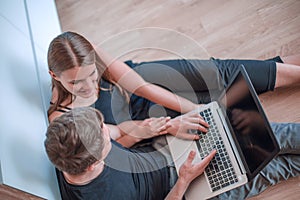 young couple with laptop sitting on the floor