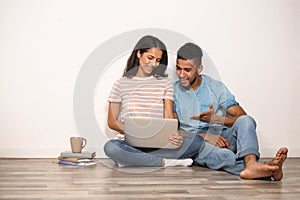 Young couple with laptop sitting on floor near light wall