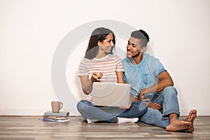 Young couple with laptop sitting on floor near light wall