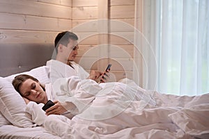 Young couple laying in bed and looking at smartphones screens