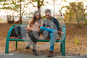 Young couple listening to music,smiling,looking at the phone and sitting on a bench in park