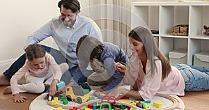 Young couple with little kids play railroad and wooden cubes