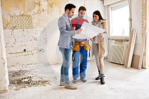 Young couple looking blueprints of their home with handyman