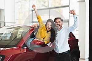 Young couple looking for car in dealership center beautiful woman is sticking out the vehicle window handsome man is