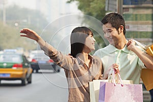 Young couple looking at each other with shopping bags hailing a taxicab in Beijing