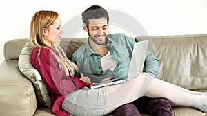 Young couple lounging on couch with laptop at home