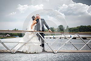 Young couple in love the bride and groom with a bouquet posing on a background pier with yachts