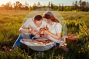 Young couple in love eating pizza and chatting outside. Woman and man having romantic picnic at sunset. Lifestyle