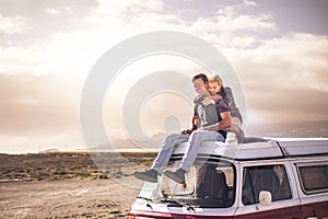 Young couple in love enjoying the travel on a vintage van during a golden sunset in a scenic place together hugging and smiling -