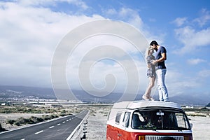 Young couple in love enjoying the travel on a vintage van standing on the roof and hugging with kiss - youth people in outdoor