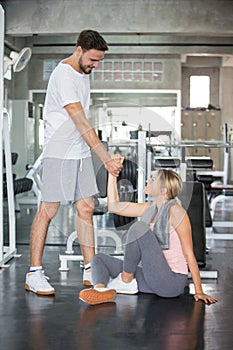 young couple in love exercise together in fitness gym . sport man boyfriend helping girlfriend to stand up or get up from floor.