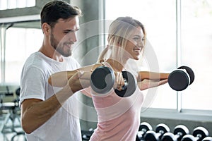young couple in love exercising weight lifting dumbbells together in fitness gym . sport man boyfriend help girlfriend workout .
