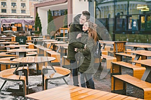 A young couple in love and a girl and a student stand embracing near the tables of a street terrace cafe closed empty without