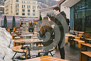 A young couple in love and a girl and a student stand embracing near the tables of a street terrace cafe closed empty without