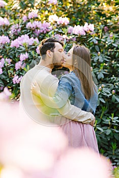 A young couple in love guy and girl kiss on the background of a rhododendron in bloom