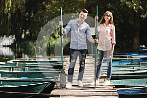 Young couple in love having fun with oars on the wooden bridge. stylish woman and man enjoy canoeing on sunny lake