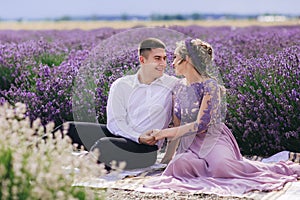 Young couple in love hugging and sitting in a lavender field on summer clody day. girl in a luxurious purple dress and with